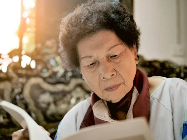 Asiatique senior femme lecture un livre avec fenêtre lumière, style de vie c — Photo