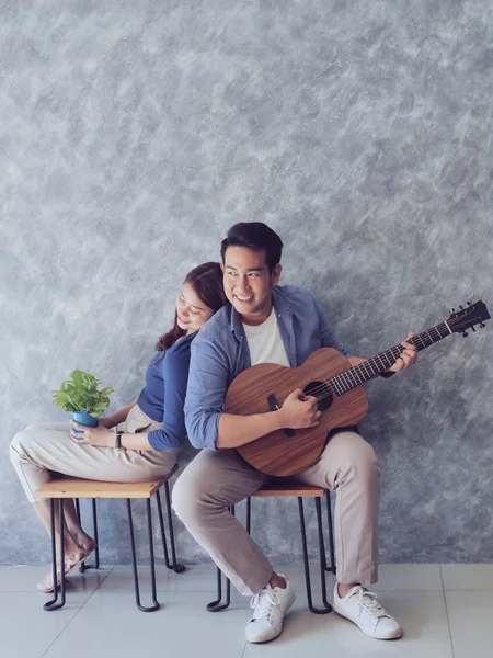 Feliz ásia casal sentado perto de parede e jogar guitarra em casa , — Fotografia de Stock