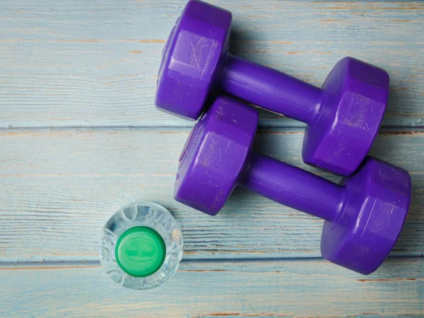 Paarse dumbbells en een fles water op blauwe houten achtergrond — Stockfoto