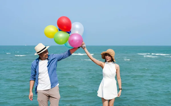 Ασιατικό ζευγάρι κρατώντας πολύχρωμα μπαλόνια στην παραλία την ηλιόλουστη μέρα — Φωτογραφία Αρχείου