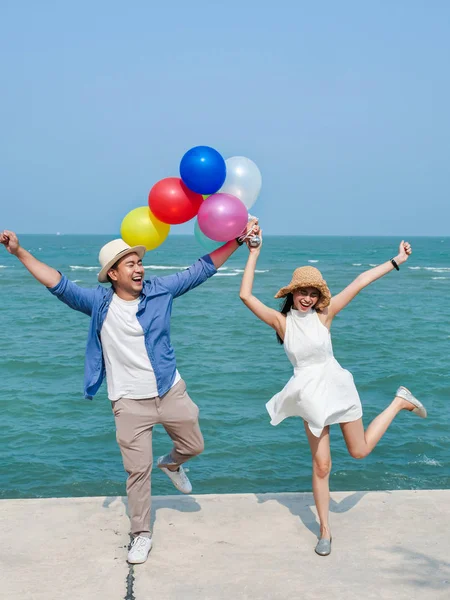 Asian couple holding colorful balloons on the beach in sunny day — Stock Photo, Image