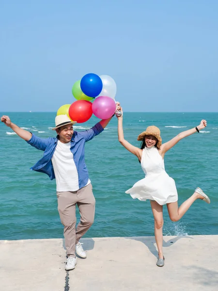 Couple asiatique tenant des ballons colorés sur la plage dans la journée ensoleillée — Photo