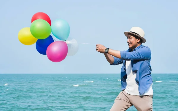 Asian Mężczyzna ciągnie kolorowe balony przeciwko błękitne niebo i Ocean. — Zdjęcie stockowe