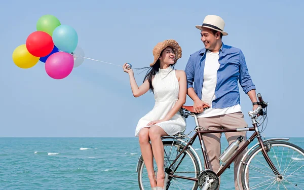 Happy Asian couple riding bicycle and holding colorful balloons