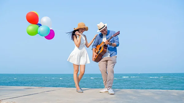 Joyeux couple jouant de la guitare et tenant des ballons sur la plage, l — Photo