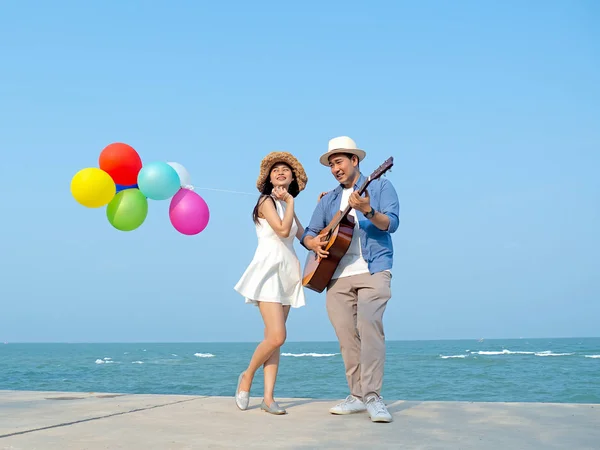 Feliz pareja tocando la guitarra y sosteniendo globos en la playa, l — Foto de Stock