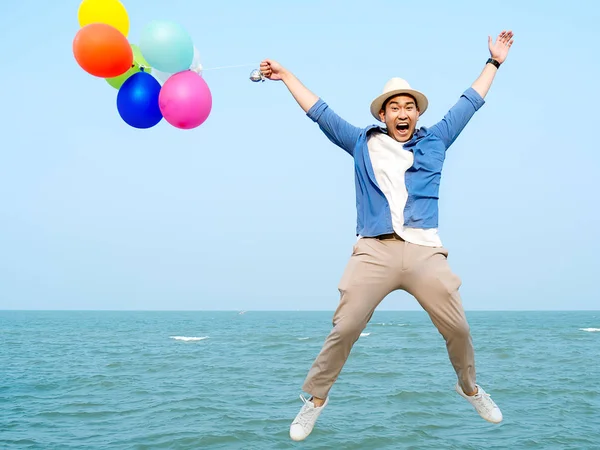 Ευτυχισμένος Ασιάτης άνθρωπος κρατώντας πολύχρωμα μπαλόνια και άλμα εναντίον BL — Φωτογραφία Αρχείου
