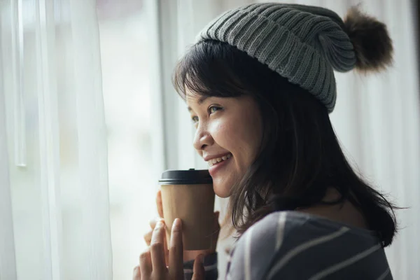 Mujer asiática feliz usando suéter y sombrero, sosteniendo taza de café ne —  Fotos de Stock