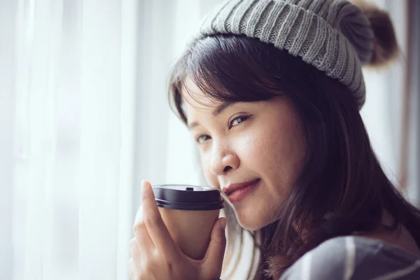 Mujer asiática feliz usando suéter y sombrero, sosteniendo taza de café ne —  Fotos de Stock