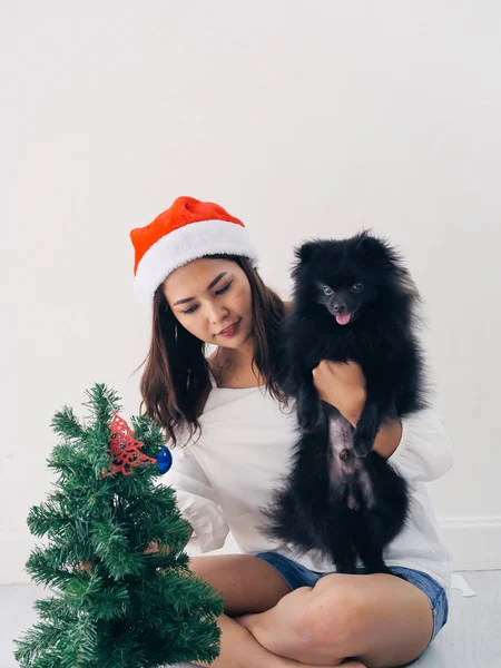 Happy Asian woman and her black dog decorating  christmas tree, — Stock Photo, Image