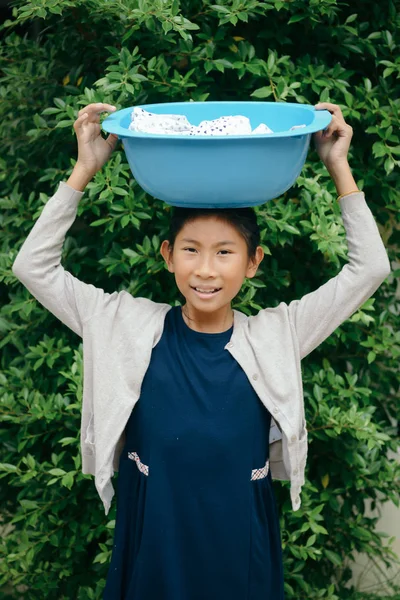 Asian girl holding blue clothes basin with green tree background — Stock Photo, Image