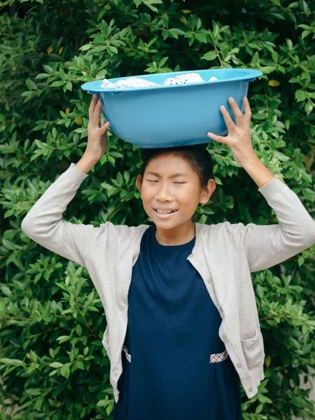 Asian girl holding blue clothes basin with green tree background — Stock Photo, Image