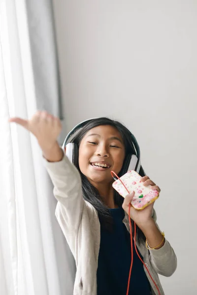 Menina asiática feliz usando smartphone e cantando uma música perto da janela — Fotografia de Stock