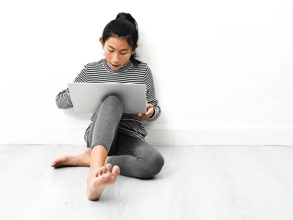 Азиатская девочка, сидящая на полу и использующая ноутбук дома . — стоковое фото