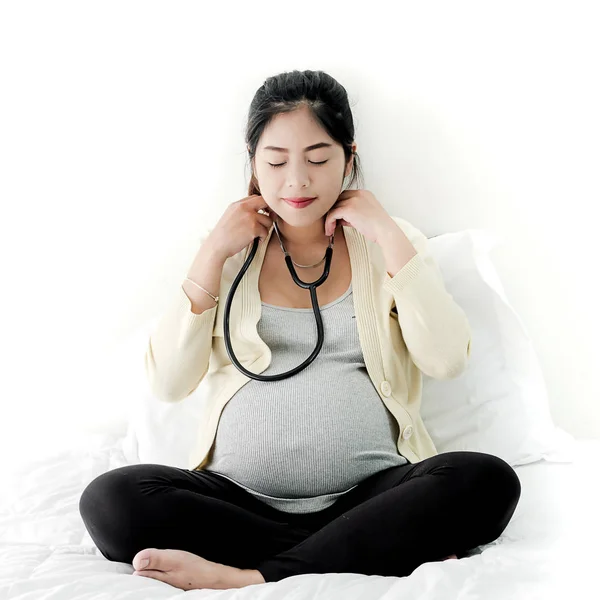 Счастливая беременная азиатка носит стетоскоп для прослушивания звука — стоковое фото