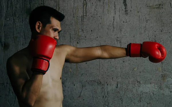 Asiático boxer com luva vermelha de pé contra a parede de cimento, baixa lig — Fotografia de Stock