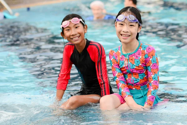 Happy Asian girls in swimming suit sitting at pool together, lif — Stock Photo, Image