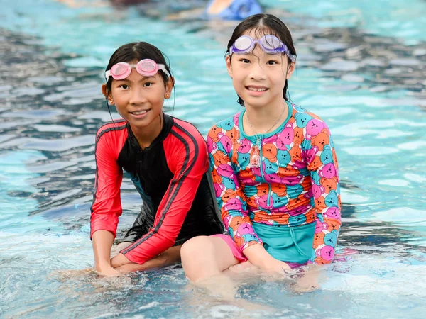 Happy Asian girls in swimming suit sitting at pool together, lif — Stock Photo, Image