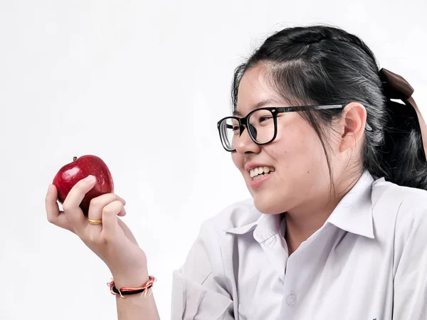 Asiatisk Schoolgirl i thailändsk Uniform ser rött äpple i hennes hand o — Stockfoto