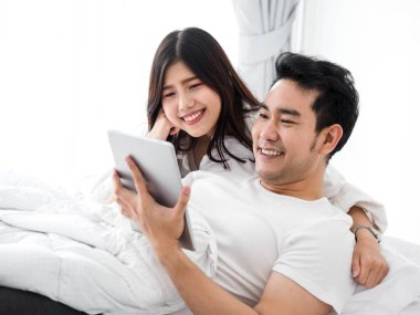 Dizüstü ve tablet birlikte yatakta ho kullanarak mutlu Asya çift