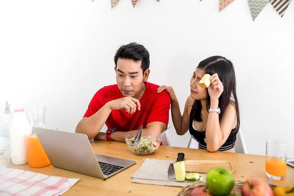 Feliz casal asiático usando laptop e comer salada e frutas frescas — Fotografia de Stock