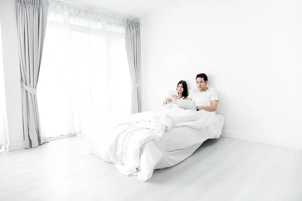 Happy Asian couple using laptop and tablet together on bed at ho — Stock Photo, Image