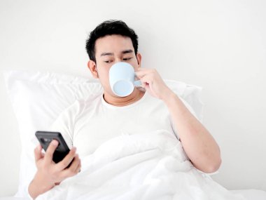 Mutlu Asya adam kullanarak akıllı telefon ve içme kahve üzerinde yatak, adam