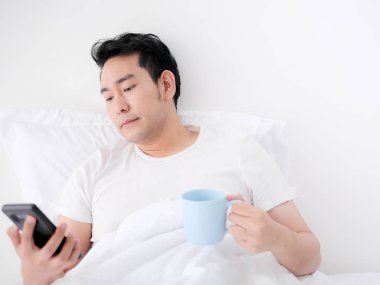 Mutlu Asya adam kullanarak akıllı telefon ve içme kahve üzerinde yatak, adam
