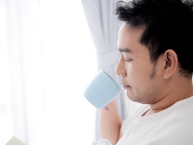 Bir kitap okuma ve yatak, adam l kahve içme mutlu Asyalı adam