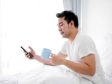 Mutlu Asya adam kullanarak akıllı telefon ve içme kahve üzerinde yatak, adam