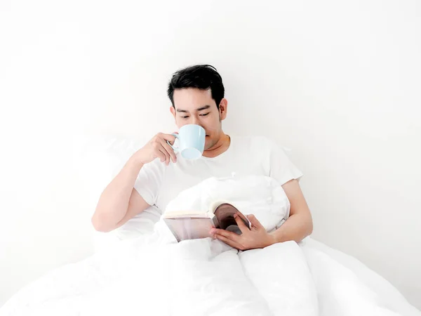 Pria Asia bahagia membaca buku dan minum kopi di tempat tidur, man l — Stok Foto