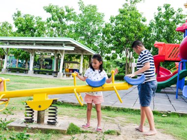 Mutlu Asyalı çocuklar parkta birlikte tahterevalli tahtası oynarken o