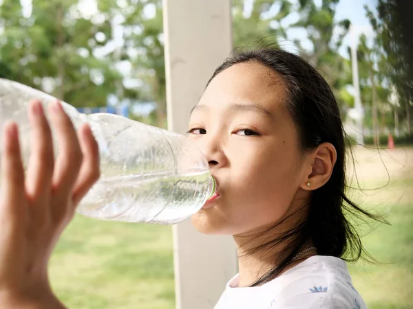 Asian girl drinking a bottle of water outdoor.