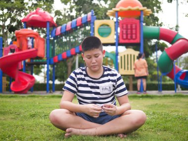 Sıkıcı Asya preteen çocuk oyun alanı ile yeşil çim üzerinde oturan