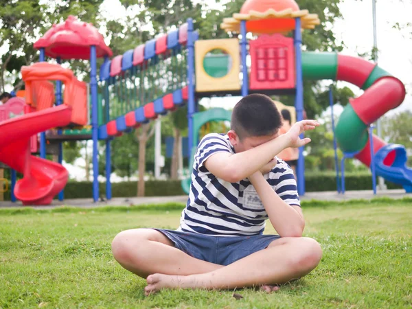 遊び場で緑の草の上に座って泣くアジアの十代の少年 — ストック写真