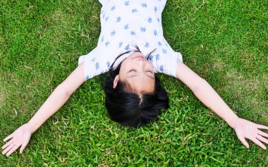 Asyalı kız açık yeşil çim üzerinde yatan ve gözlerini kapattı