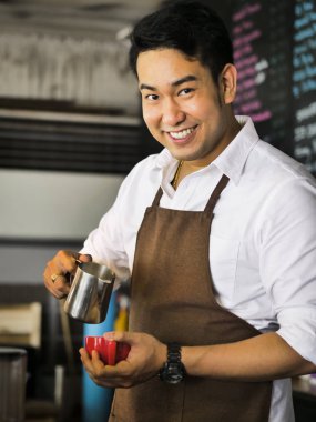 Mutlu Asya barista latte için kırmızı kahve fincanı içine süt dökme bir