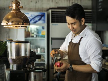Mutlu Asya barista latte için kırmızı kahve fincanı içine süt dökme bir