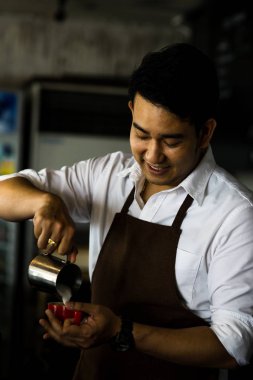 Mutlu Asya barista latte için kırmızı kahve fincanı içine süt dökme bir