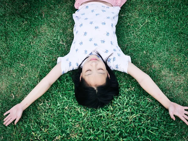 Asiática chica acostada en verde hierba al aire libre y cerrado los ojos — Foto de Stock
