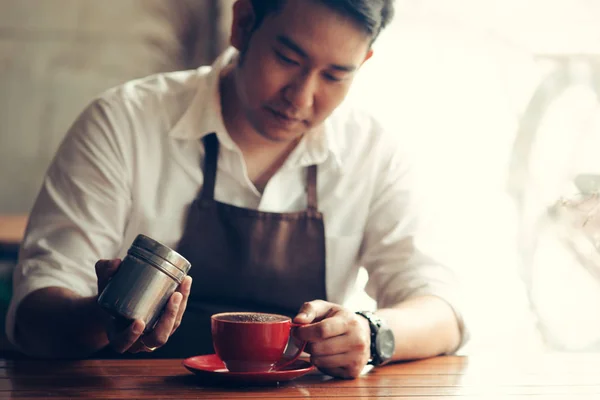 Asiático barista asperja chocolate en polvo en la bebida en rojo taza . —  Fotos de Stock