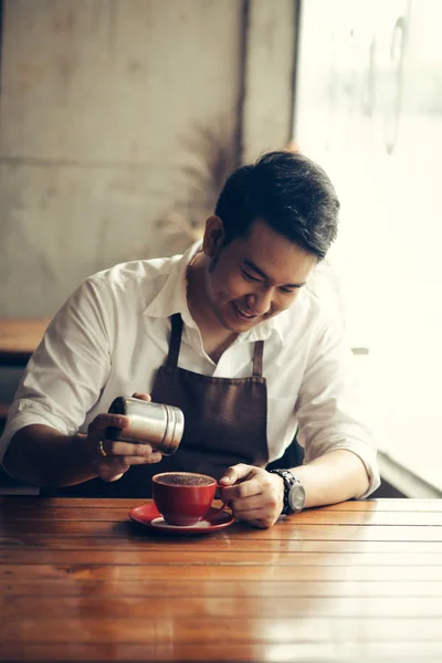 Asijské barista sype čokoládový prášek na pití v červeném poháru. — Stock fotografie