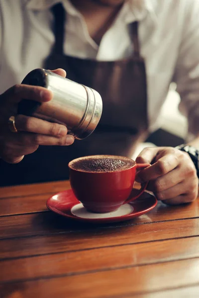 Asiático barista asperja chocolate en polvo en la bebida en rojo taza . —  Fotos de Stock