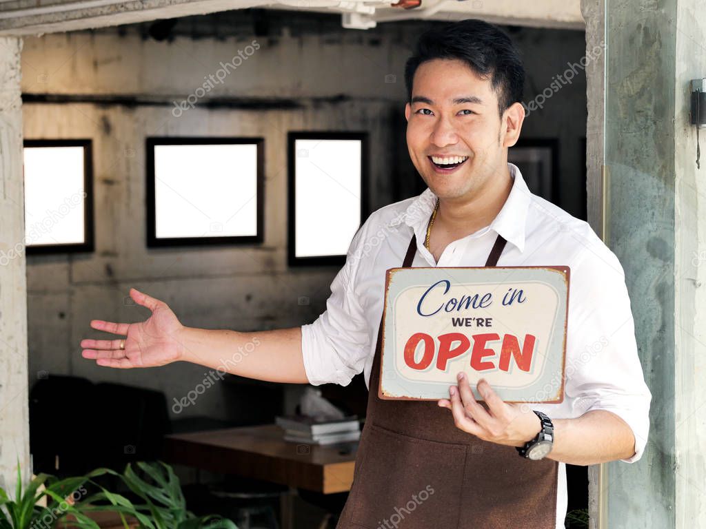 Cheerful Asian barista man holding welcome board in front of cof