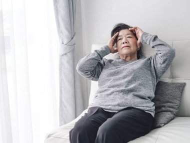 Asyalı yaşlı kadın evde kanepede otururken bir baş ağrısı var