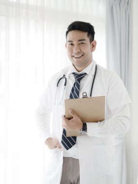 Pencerenin yanında duran mutlu kendine güvenen Asyalı doktor, yaşam tarzı con