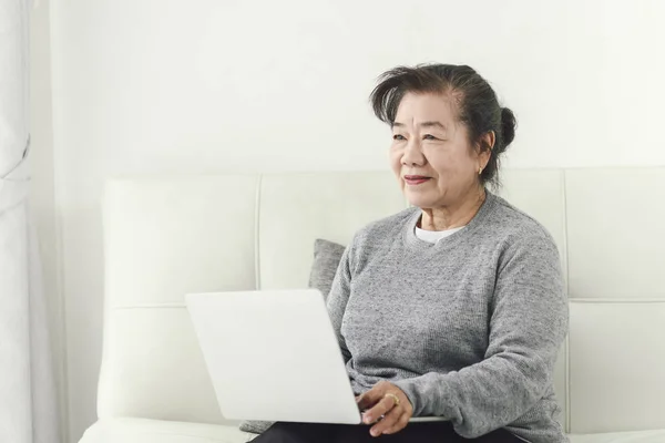 Mutlu Asya yaşlı kadın evde dizüstü bilgisayar kullanarak, yaşam tarzı kavramı — Stok fotoğraf