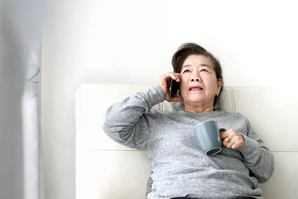 Gelukkig Aziatische Senior vrouw praten een telefoon en het houden van drankje Cup, — Stockfoto