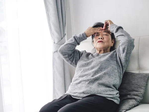 Starší asijská žena bolí hlava, když sedí na pohovce doma — Stock fotografie