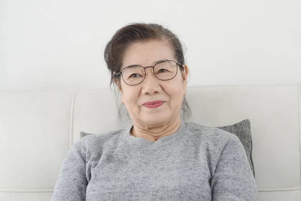 Szczęśliwy Asian starszy kobieta noszenie okulary i siedzący na sofa — Zdjęcie stockowe